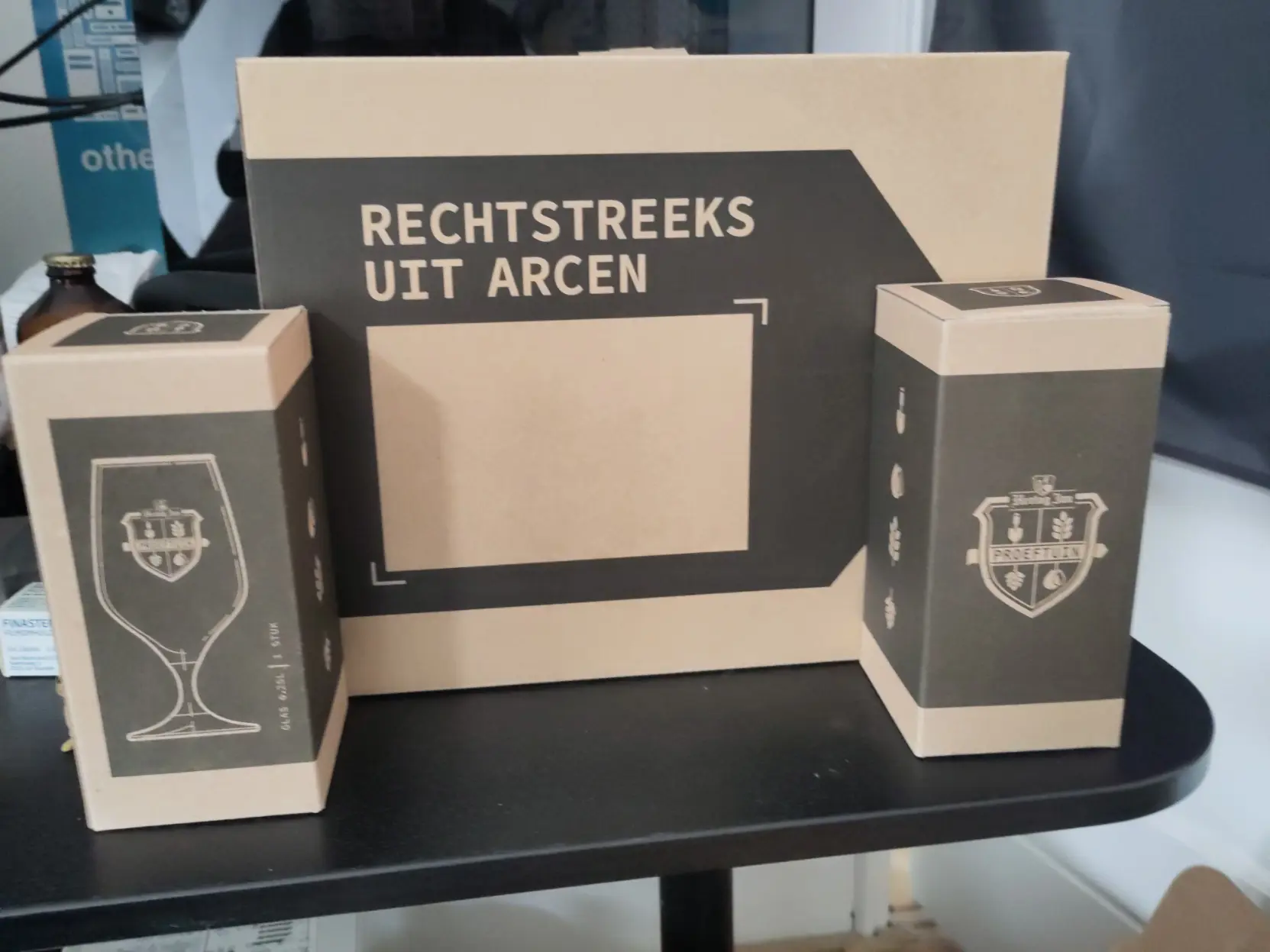 Three boxes.

The middle one says "Straight from Arcen" in Dutch.

The two smaller ones say "Proeftuin" and show a glass on it.