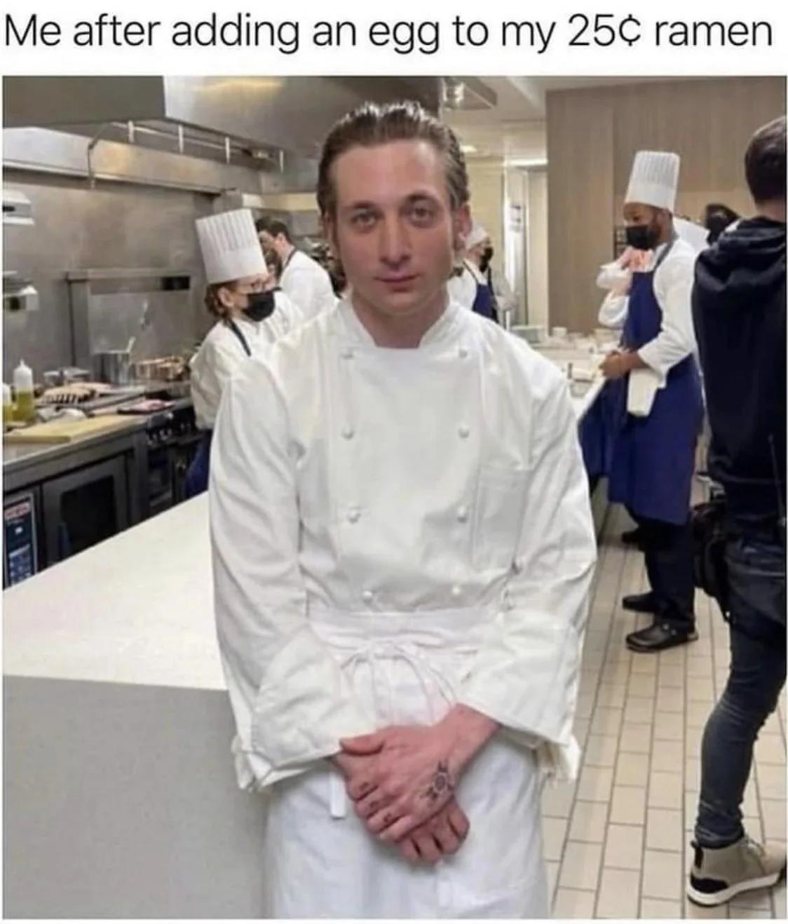 This image depicts what appears to be a newly appointed chef amidst a bustling kitchen filled with other cooks. Above the picture is the humorous caption, “Me after adding an egg to my 25-cent ramen.”